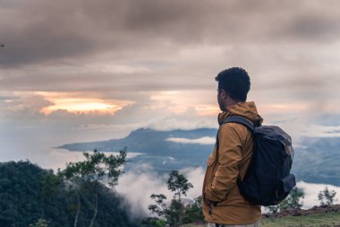 Bir gezgin, gün doğumunda sisli vadiye ve okyanusa bakarak bir dağın zirvesinde oturur. Bir sırt çantası ve ceket giyerek, huzurlu manzaranın tadını çıkarıyor, macerayı, özgürlüğü ve keşfi simgeliyor..