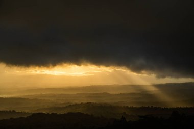 Altın gün batımında yıkanan yuvarlanan tepelerin çarpıcı manzarası dramatik kara bulutlar kontrastlar yaratıyor.