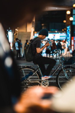 Kanazawa, Japonya - 23 Ağustos 2023: Yoğun bir Japon şehrinde gece trafik ışığı beklerken bir kişi bir bisikletin üzerinde oturuyor..
