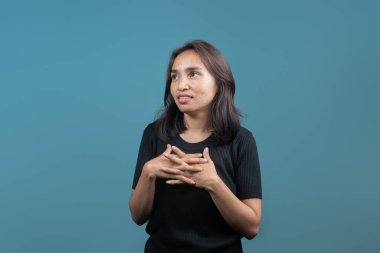 Endonezyalı bir kadın parmakları birbirine kenetlenmiş bir şekilde kurnazca gülümser ve gözleri hafifçe yukarı bakar, düşünceli ama kararsız görünür. Kararsızlık, tefekkür ya da tartma seçenekleri..