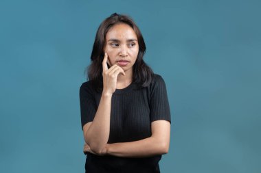 Yanağında işaret parmağı olan Endonezyalı bir kadın. Düşünceli görünüyor. Bir fikri düşünüyor ya da düşünüyor gibi. Karar verme ve tefekkürün bir konsept resmi.