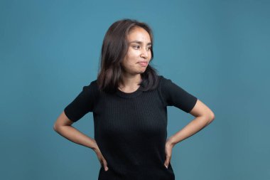 Endonezyalı bir kadın elleri kalçasında durur, gülümser ve kendinden emin bir ifadeyle yana bakar. Kendine güven, farkındalık ya da farkındalık kavramı..