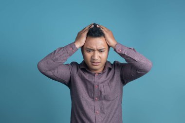 Hayal kırıklığına uğramış Endonezyalı bir adam, iki eli başının üstünde, bunalmış ve stresli görünüyor. Günlük hayatta ya da işte panik, karışıklık, tükenme ya da zihinsel baskının sembolü.