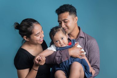 Mutlu Endonezyalı ebeveynler stüdyo ortamında kızlarına sevgi ve özenle sarılıyorlar. Aile bağlarını, ebeveynliklerini ve sevgilerini gösteren sıcak, duygusal bir an..