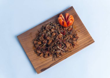 Geleneksel baharatlı Endonezya yemeği, dilimlenmiş domateslerle süslenmiş ahşap bir tabakta servis edilen kızarmış ançüez ve tempeh. Mutfak, yemek ve kültürel içerik için mükemmel..