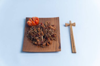 Geleneksel baharatlı Endonezya yemeği, dilimlenmiş domateslerle süslenmiş ahşap bir tabakta servis edilen kızarmış ançüez ve tempeh. Mutfak, yemek ve kültürel içerik için mükemmel..