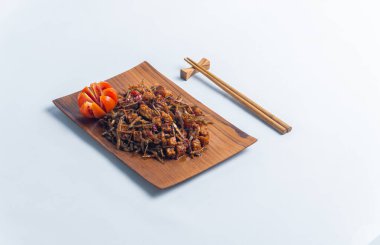 Geleneksel baharatlı Endonezya yemeği, dilimlenmiş domateslerle süslenmiş ahşap bir tabakta servis edilen kızarmış ançüez ve tempeh. Mutfak, yemek ve kültürel içerik için mükemmel..