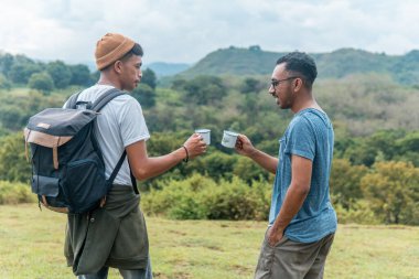 İki neşeli adam çimenli tepede oturmuş, gülüyor ve bardakları tokuşturuyorlar. Neşeli bir arkadaşlık, seyahat ve doğada yakalanan boş bir zaman..