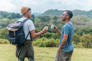 İki neşeli adam çimenli tepede oturmuş, gülüyor ve bardakları tokuşturuyorlar. Neşeli bir arkadaşlık, seyahat ve doğada yakalanan boş bir zaman..