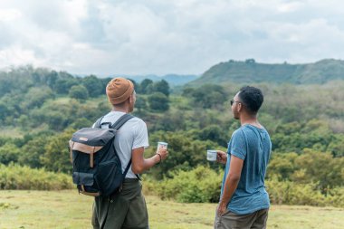 İki Endonezyalı adam kamp gezisinde bir fincan kahve içiyorlar.
