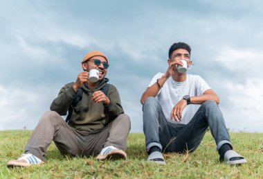 İki neşeli adam çimenli tepede oturmuş, gülüyor ve bardakları tokuşturuyorlar. Neşeli bir arkadaşlık, seyahat ve doğada yakalanan boş bir zaman..