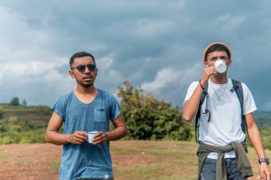 İki Endonezyalı adam kamp gezisinde bir fincan kahve içiyorlar.