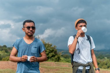 İki Endonezyalı adam kamp gezisinde bir fincan kahve içiyorlar.