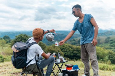 İki Endonezyalı adam kamp gezisinde bir fincan kahve içiyorlar.