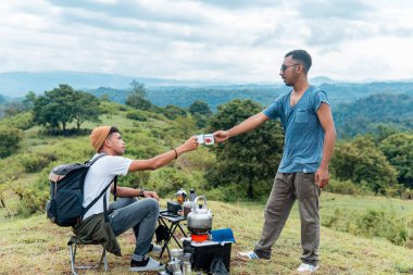 İki Endonezyalı adam kamp gezisinde bir fincan kahve içiyorlar.
