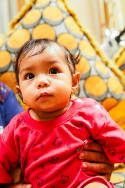 Kırmızı elbiseli sevimli bebek elinde oyuncak tutarken ve çiğnerken kanepede oturuyor. Ebeveynlik, çocukluk, bebek ürünleri veya sağlıkla ilgili içerik için mükemmel yakın çekim görüntüleri.
