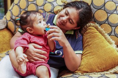 Annesinin kanepesinde otururken küçük bir oyuncakla oynayan küçük bir kızın yakın çekimi. Ev içi aile hayatı ve bağlılık..