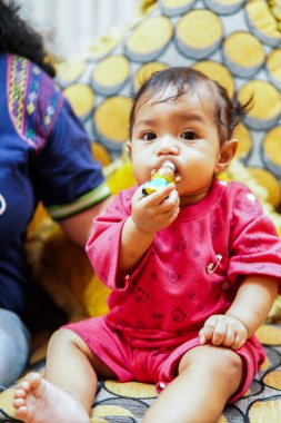 Kırmızı elbiseli sevimli bebek elinde oyuncak tutarken ve çiğnerken kanepede oturuyor. Ebeveynlik, çocukluk, bebek ürünleri veya sağlıkla ilgili içerik için mükemmel yakın çekim görüntüleri.