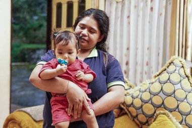 Annesinin kanepesinde otururken küçük bir oyuncakla oynayan küçük bir kızın yakın çekimi. Ev içi aile hayatı ve bağlılık..