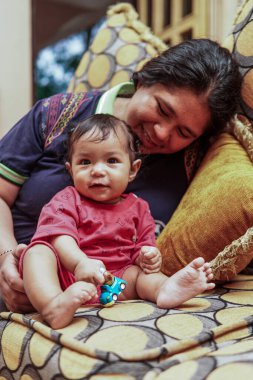 Annesinin kanepesinde otururken küçük bir oyuncakla oynayan küçük bir kızın yakın çekimi. Ev içi aile hayatı ve bağlılık..