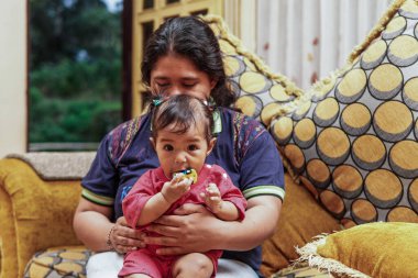 Annesinin kanepesinde otururken küçük bir oyuncakla oynayan küçük bir kızın yakın çekimi. Ev içi aile hayatı ve bağlılık..