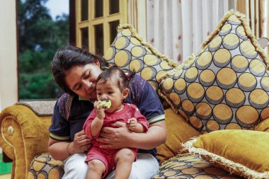 Genç bir anne, parlak ve renkli bir kanepede sevgi, neşe ve gerçek aile bağını gösteren, küçük kızıyla evde oynar..