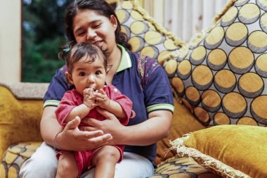 Genç bir anne, parlak ve renkli bir kanepede sevgi, neşe ve gerçek aile bağını gösteren, küçük kızıyla evde oynar..
