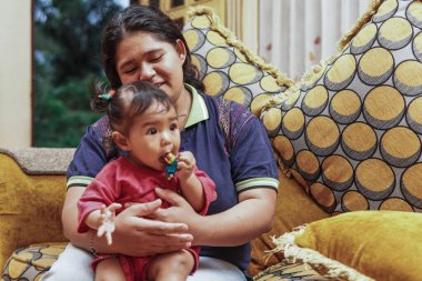Genç bir anne, parlak ve renkli bir kanepede sevgi, neşe ve gerçek aile bağını gösteren, küçük kızıyla evde oynar..
