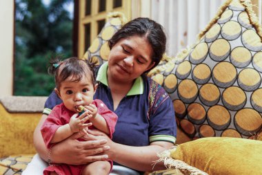 Genç bir anne, parlak ve renkli bir kanepede sevgi, neşe ve gerçek aile bağını gösteren, küçük kızıyla evde oynar..