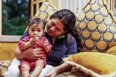 Genç bir anne, parlak ve renkli bir kanepede sevgi, neşe ve gerçek aile bağını gösteren, küçük kızıyla evde oynar..