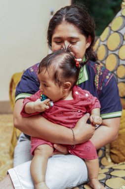 Genç bir anne, parlak ve renkli bir kanepede sevgi, neşe ve gerçek aile bağını gösteren, küçük kızıyla evde oynar..