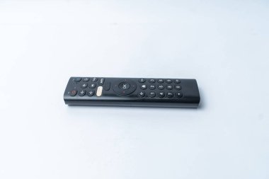Teknoloji, elektronik veya kullanıcı arayüzü temaları için ideal, beyaz bir yüzey üzerinde uzanan siyah TV uzaktan kumandasının minimalist görüntüsü.