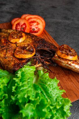 Izgara balık taze marul, domates dilimleri ve limonlu garnitürle servis edilir. Deniz ürünleri, sağlıklı beslenme, mutfak temaları, restoran menüsü tasarımı ve geleneksel mutfak için mükemmel..