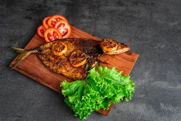 Izgara balık taze marul, domates dilimleri ve limonlu garnitürle servis edilir. Deniz ürünleri, sağlıklı beslenme, mutfak temaları, restoran menüsü tasarımı ve geleneksel mutfak için mükemmel..