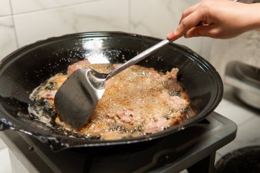 Siyah bir tavada kızgın yağda kızartılan, metal bir spatulayla karıştırılmış çiğ domuz eti. Geleneksel Asya yemek pişirme süreci ev mutfağında otantik mutfak hazırlıklarını gösteriyor.