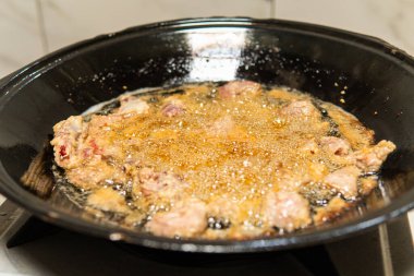 Siyah bir tavada kızgın yağda kızartılan, metal bir spatulayla karıştırılmış çiğ domuz eti. Geleneksel Asya yemek pişirme süreci ev mutfağında otantik mutfak hazırlıklarını gösteriyor.