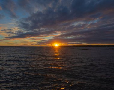 Arka planda, denizin üstünde gün batımı.