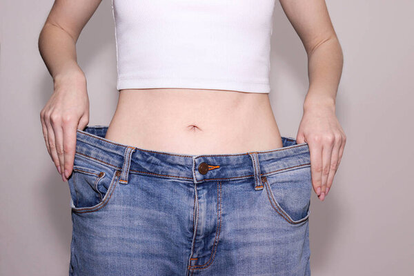 Успешная потеря веса. Тонкая женщина в огромных джинсах. Здоровье и питание.