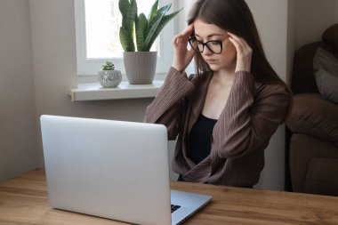 Çok çalışan genç bir kadın, serbest çalışan, bilgisayarla uğraşırken baş ağrısı çeken şakaklarına masaj yapan bir ofis çalışanı..