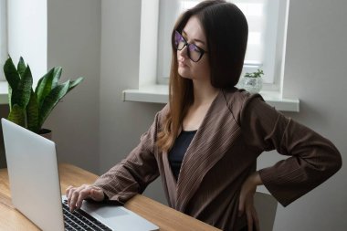 Yorgun kadın ofis çalışanı, bilgisayar ve dizüstü bilgisayarla uğraşırken sırt ağrısı çeken serbest çalışan. Ofis sendromunun belirtileri