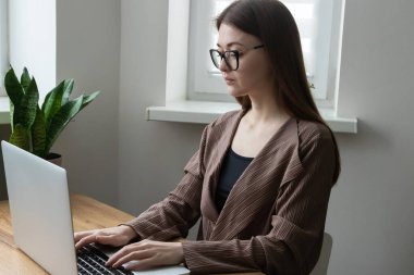Gözlüklü, bilgisayarla çalışan, evden dizüstü bilgisayar kullanan serbest çalışan genç bir kadın..