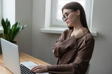 Yorgun kadın ofis çalışanı, bilgisayar ve dizüstü bilgisayarla uğraşırken boynu, omzu ağrıyan serbest çalışan. Ofis sendromunun belirtileri