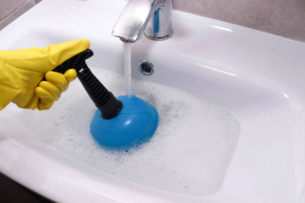 Woman hands unclogging bathroom sink with plunger. Overflowing bathroom sink. Clogged drain.