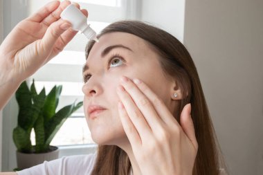 Genç bir kadın, yanmayı, kaşıntıyı ve kaşıntıyı azaltmak için nemlendirici göz damlası kullanıyor. Görüş bakımı, kuru göz sendromu ve alerji nöbeti kavramı.