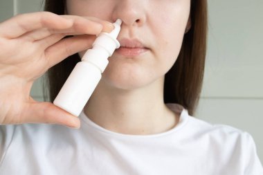 Burun spreyi kullanan genç bir kadın tıkanıklığı gidermek için, mevsimsel alerjiler, burun akıntısı.