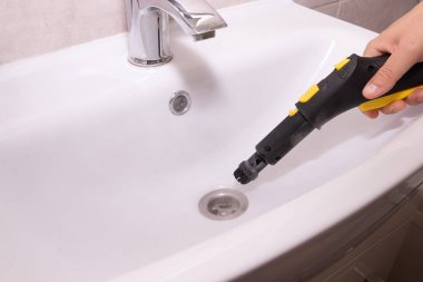 Ev temizleme konsepti: banyo lavabosu giderini ve çevresindeki alanı temizlemek ve sterilize etmek için buhar temizleyicisi kullanmak. Çevre dostu ev hijyeni.