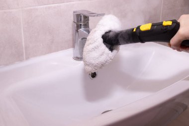 Lavabo musluğunu temizlemek ve dezenfekte etmek için buhar temizleyicisi kullanmak. ev temizliği, çevre temizliği ve ev bakımı konuları.