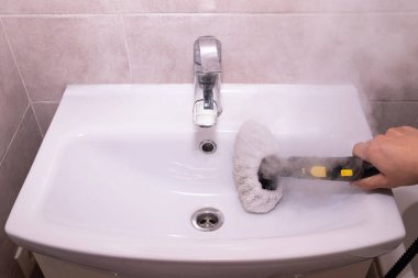 Ev temizleme konsepti: banyo lavabosunu temizlemek ve sterilize etmek için buhar temizleyicisi kullanmak. Çevre dostu banyo temizliği