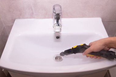 Buharlı temizleyiciyi dezenfekte etmek ve lavaboyu temizlemek için kullanmak. ev temizliği, çevre temizliği ve ev bakımı konuları.