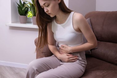 Karnını ağrısı içinde tutan yorgun genç bir kadın mide ağrısı, mide ağrısı, regl sancısı, adet sancısı, şişkinliği. Sindirim sorunları, mide iltihabı, mide ağrısı. 